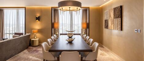 A hotel dining room with a long table, chairs, a chandelier, and a large window with curtains.