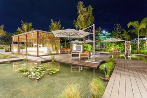 A nighttime resort pool area with a wooden deck, lounge chairs, umbrellas, and a covered seating area. - Crowne Plaza Vientiane by IHG (Vientiane)