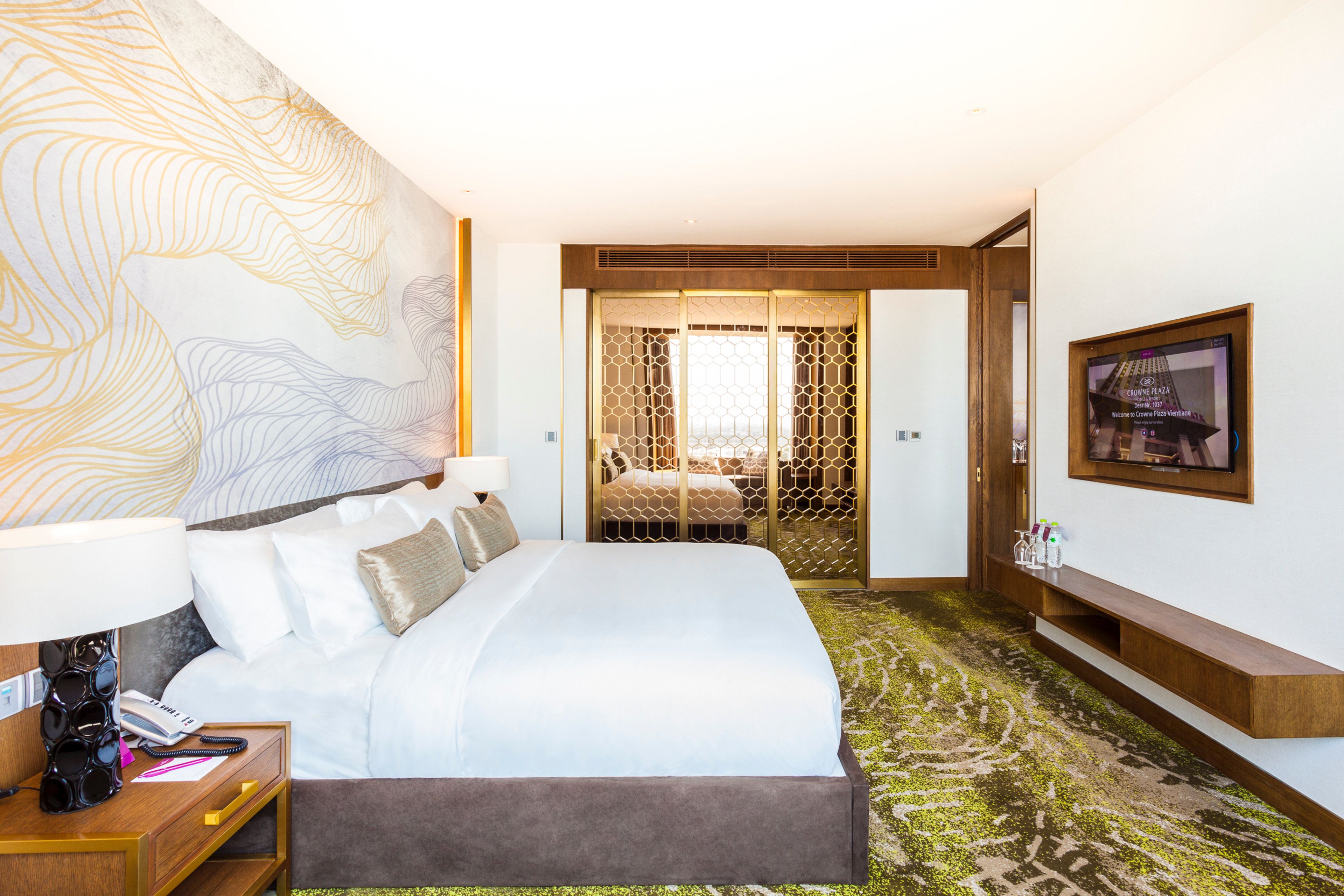 A hotel room with a large bed, a desk with a telephone, a TV mounted on the wall, and a decorative wall mural.