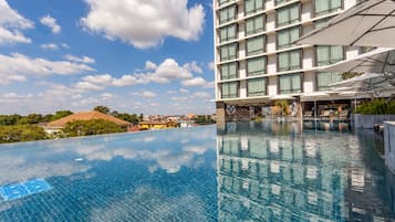 A hotel with a large outdoor swimming pool, a covered outdoor area with umbrellas, and a view of the surrounding neighborhood.