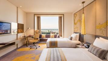 A hotel room with a bed, desk, chair, television, and a view of the city.