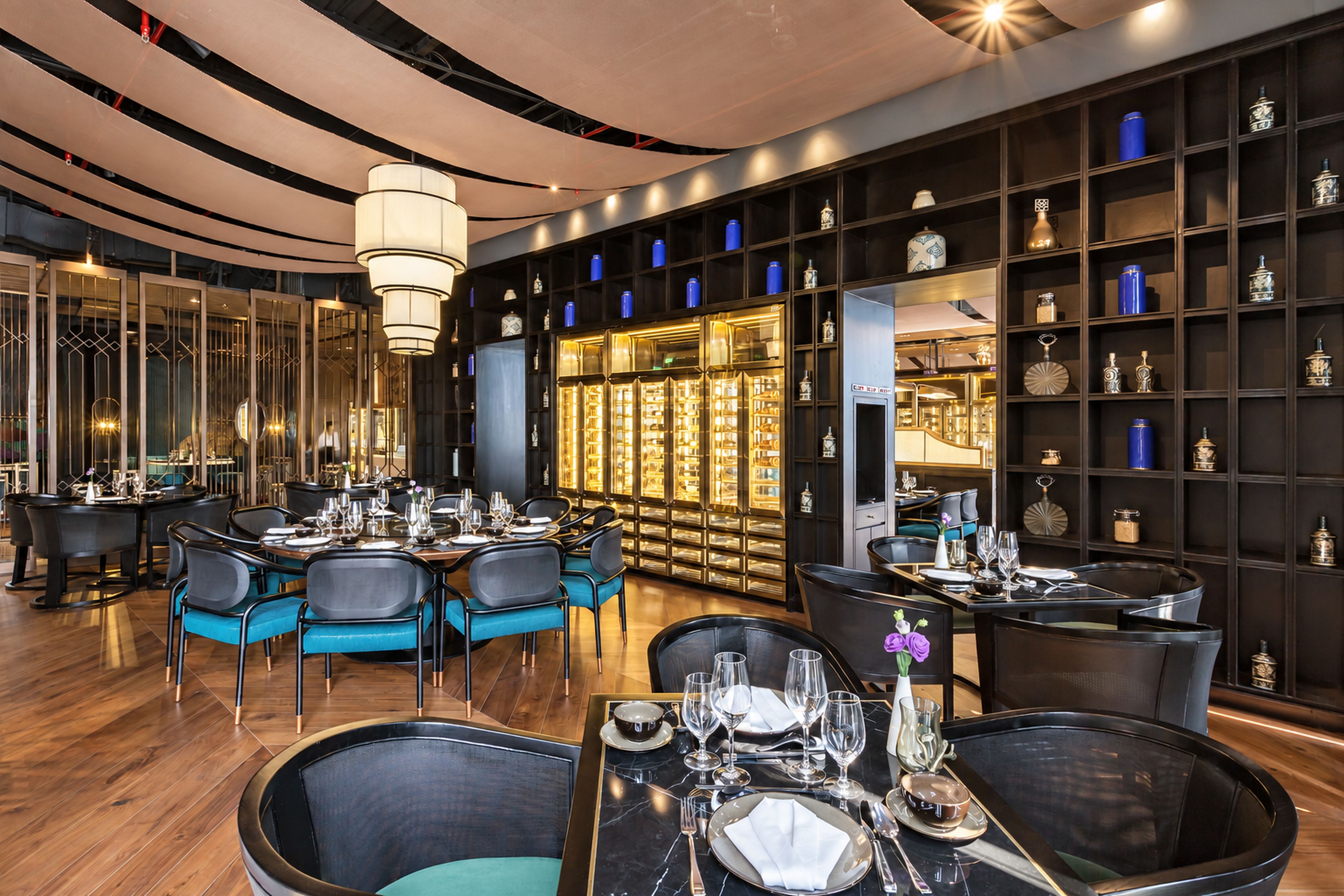 A restaurant interior with round tables, blue chairs, and a display of blue vases on shelves.