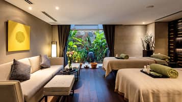 Habitación de hotel con sofá, una mesita, cama, ventana con cortinas y vistas al exterior con vegetación.