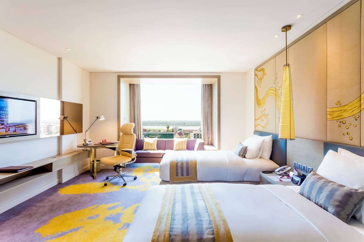 A hotel room with a large bed, a desk with a computer, a TV, and a view of the city.