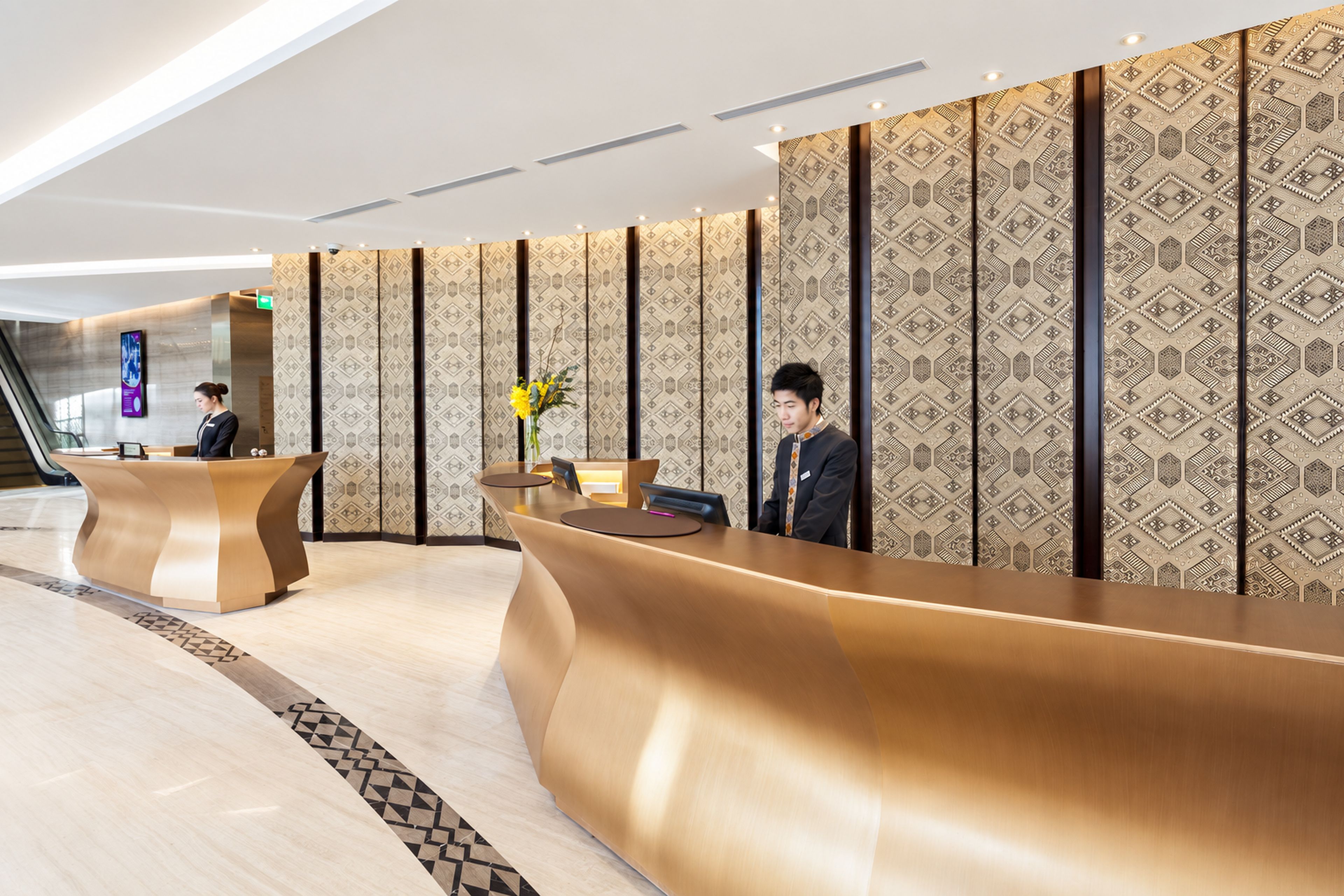 A modern reception desk with a curved design, a digital screen, and a patterned wall in the background.
