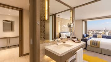 A modern hotel room with a large bed, a bathroom with a double sink, and a city view.
