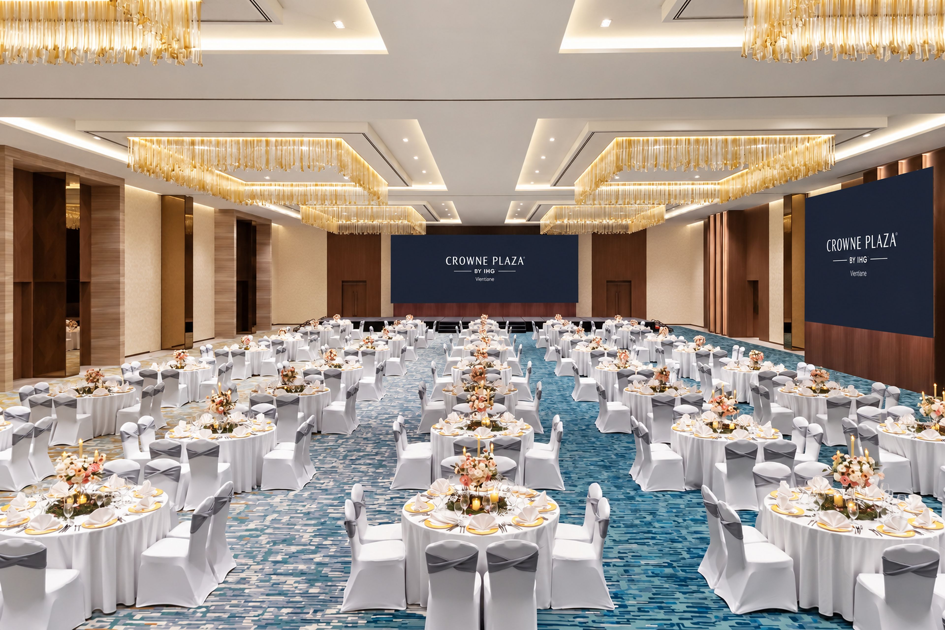 A large conference room with round tables, white chairs, and chandeliers.