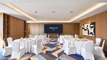Une salle de conférence équipée de tables rondes, de chaises blanches et d’un grand écran affichant le logo « CROWN PLAZA BY IHG ».