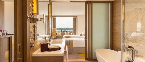 A modern hotel bathroom with a large bathtub, a vanity with a mirror, and a view of the city through the window.