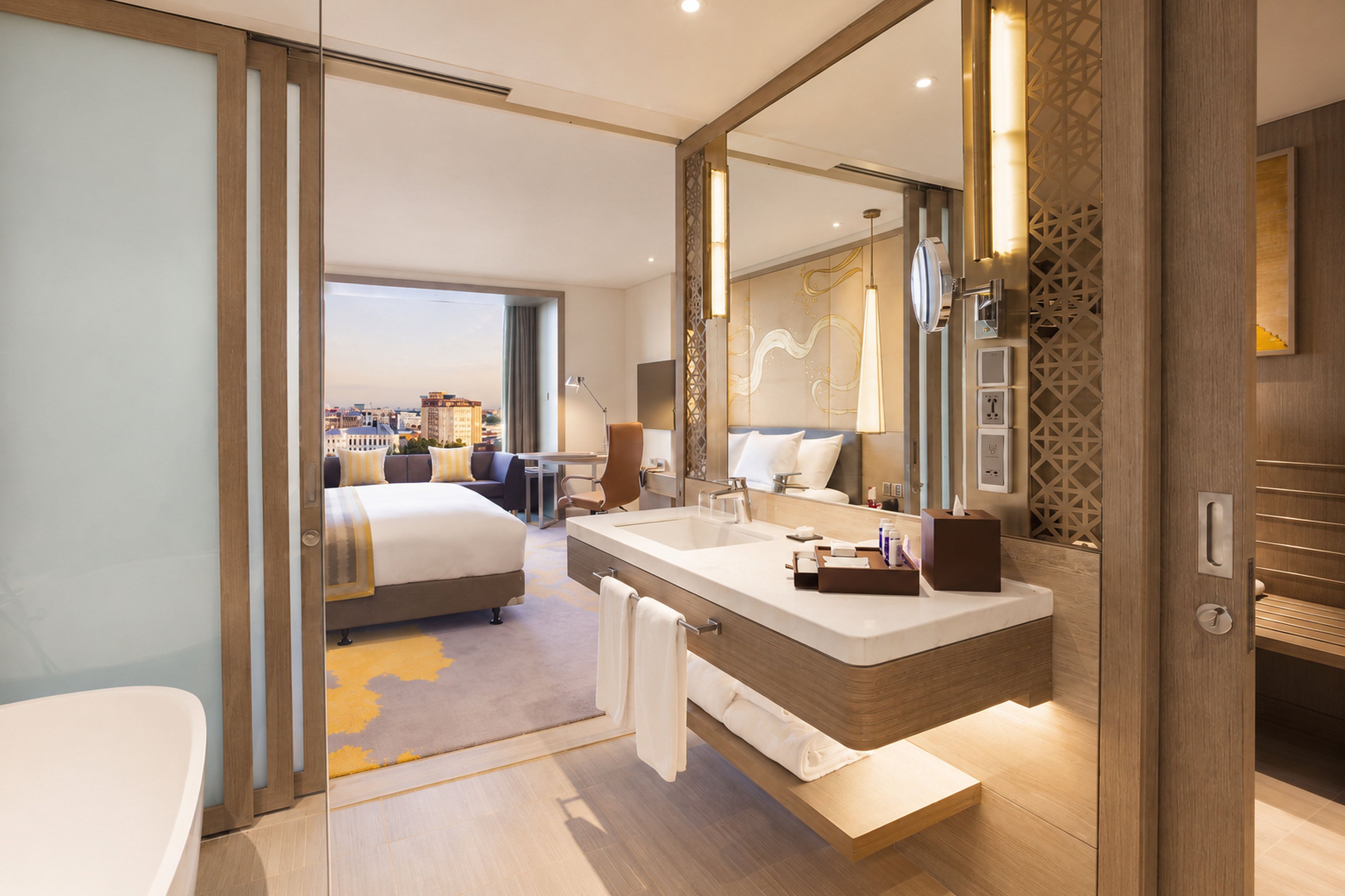 Een moderne hotelkamer met een groot bed, een badkamer met een dubbele wastafel en uitzicht op de stad.