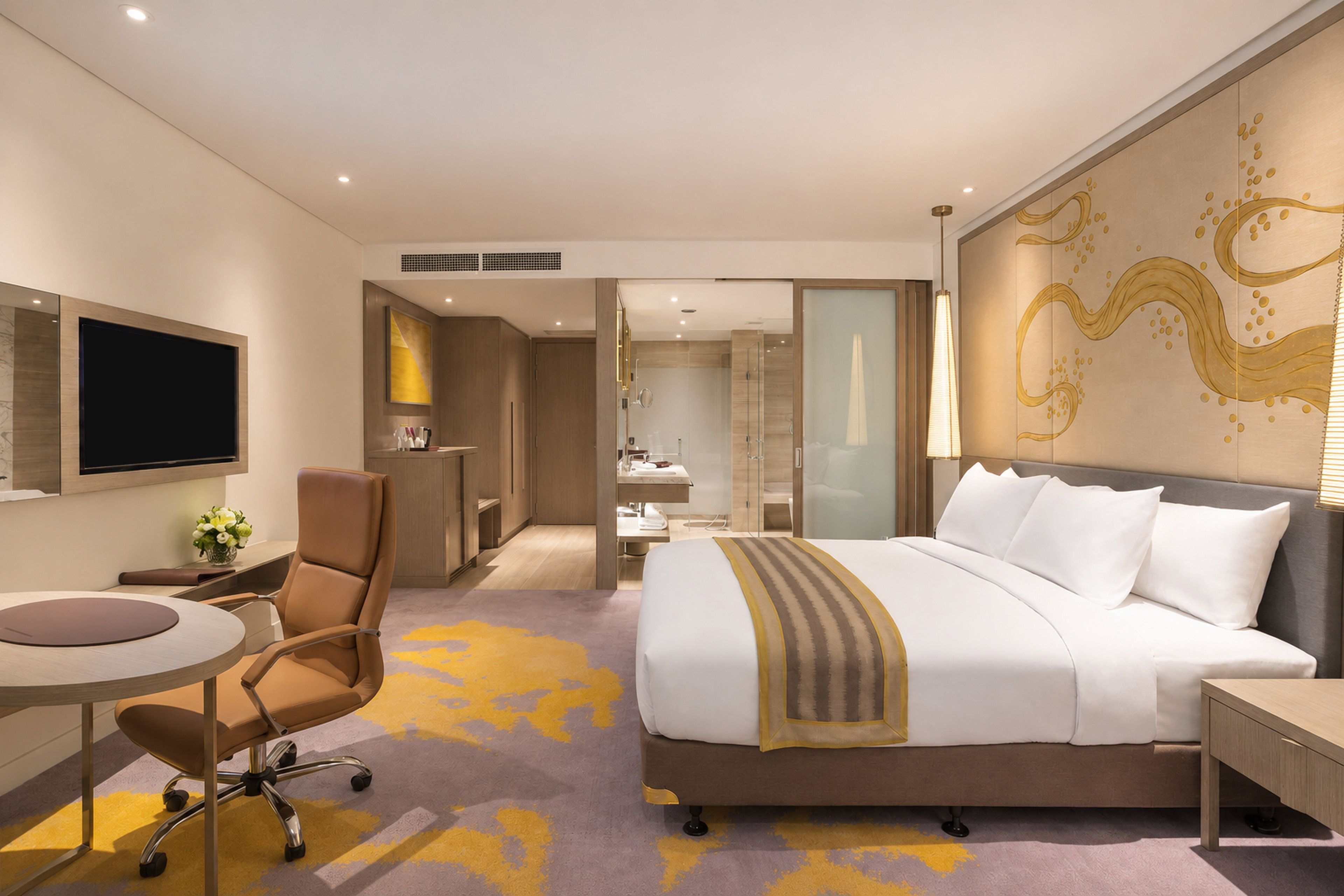 A hotel room with a bed, a desk, a chair, a TV, and a bathroom visible through an open door.