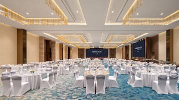 Un amplio salón de conferencias con mesas redondas, manteles blancos y sillas con cintas grises.