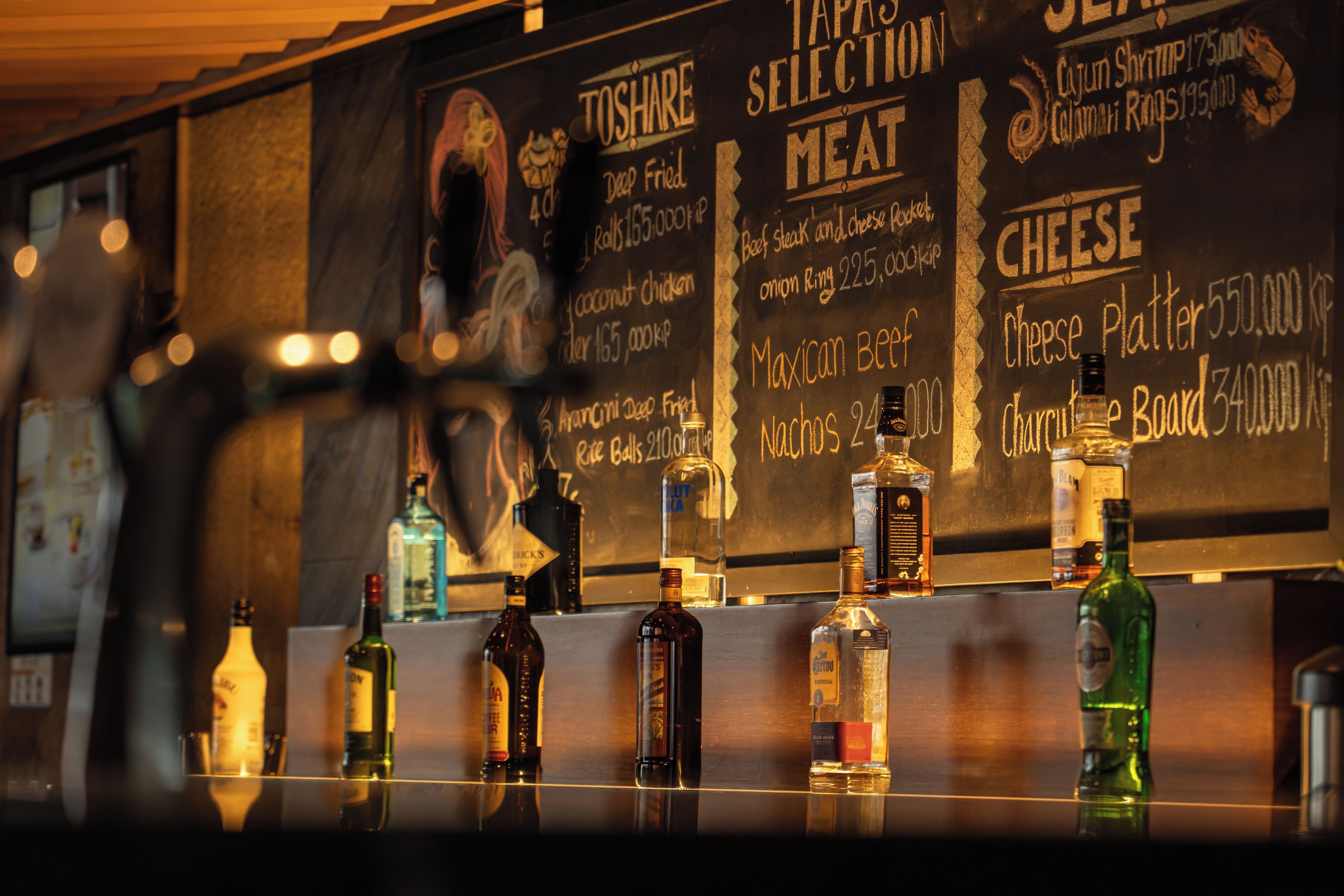 Een bar met een krijtbord waarop gerechten staan vermeld zoals 'Toshare', 'Gefrituurd' en 'Mexicaanse Beef Nachos'.