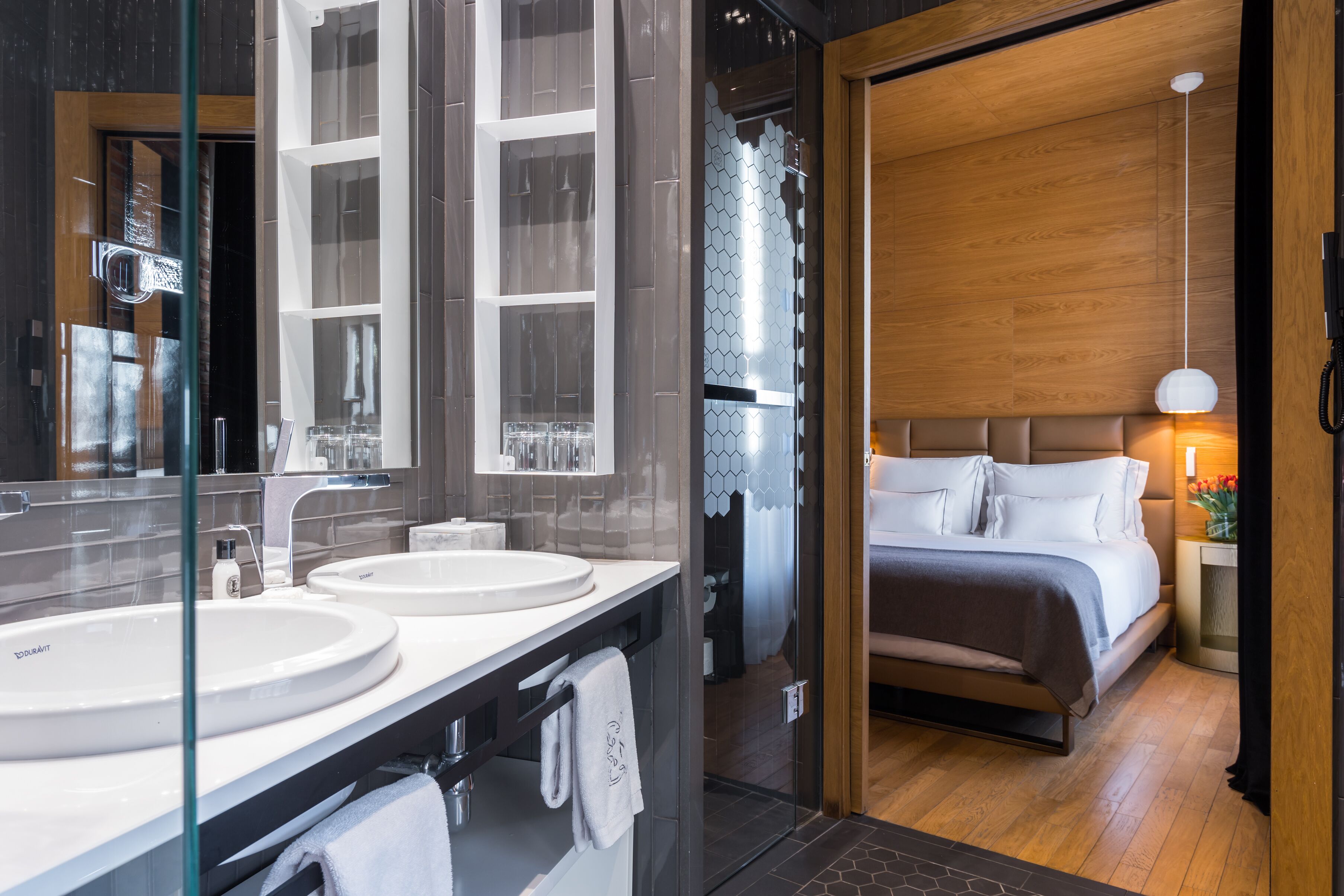 A modern bathroom with two sinks, a glass shower enclosure, and a wooden floor.