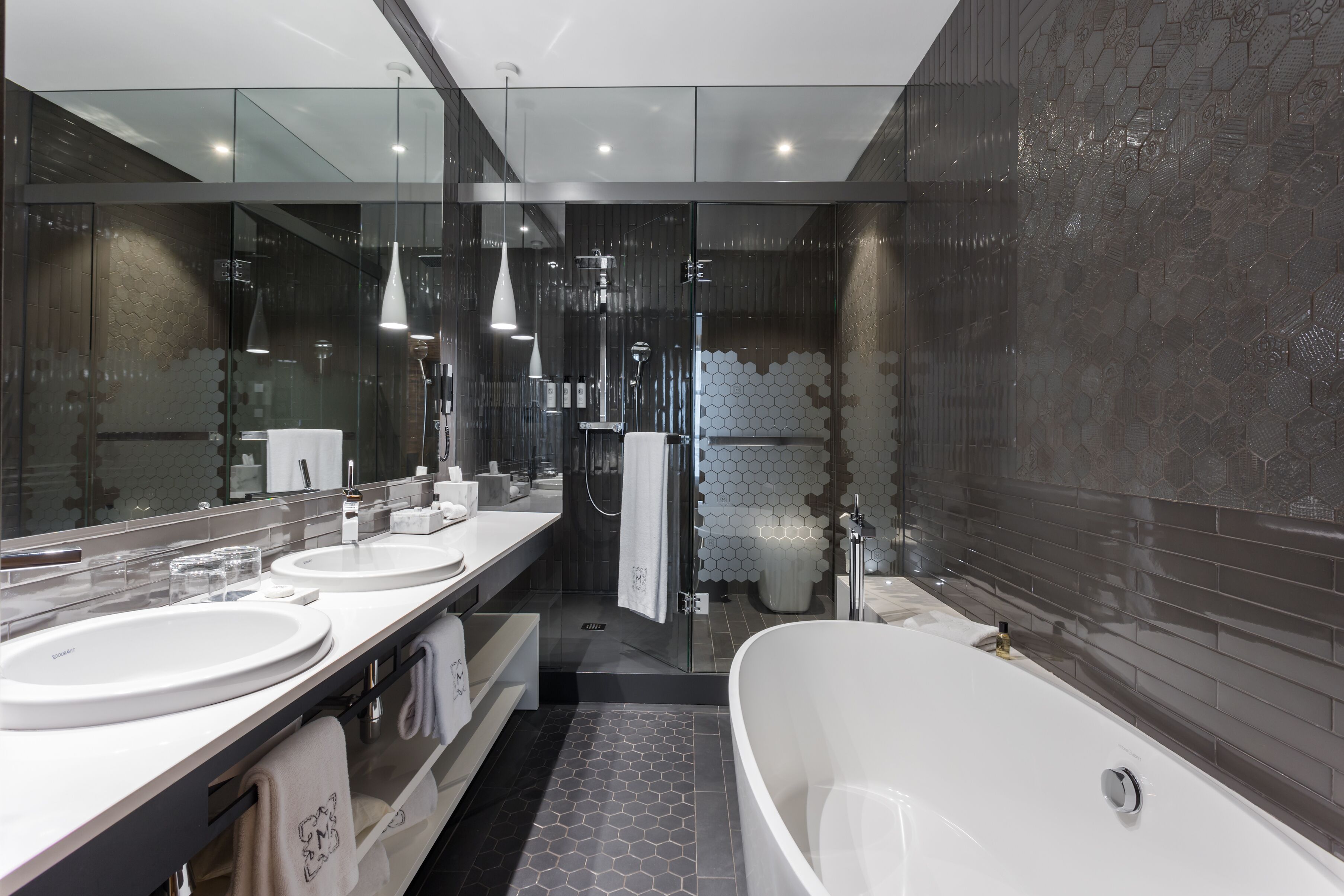 A modern bathroom with a large mirror, two sinks, a bathtub, and a glass-enclosed shower.