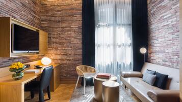 Una habitación moderna con pared de ladrillo, un escritorio con computadora, un sofá y un ventanal con cortinas translúcidas.