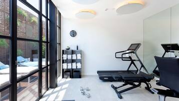 Une salle de sport moderne équipée de matériel d’exercice, dotée de grandes fenêtres et offrant une vue sur une terrasse extérieure.