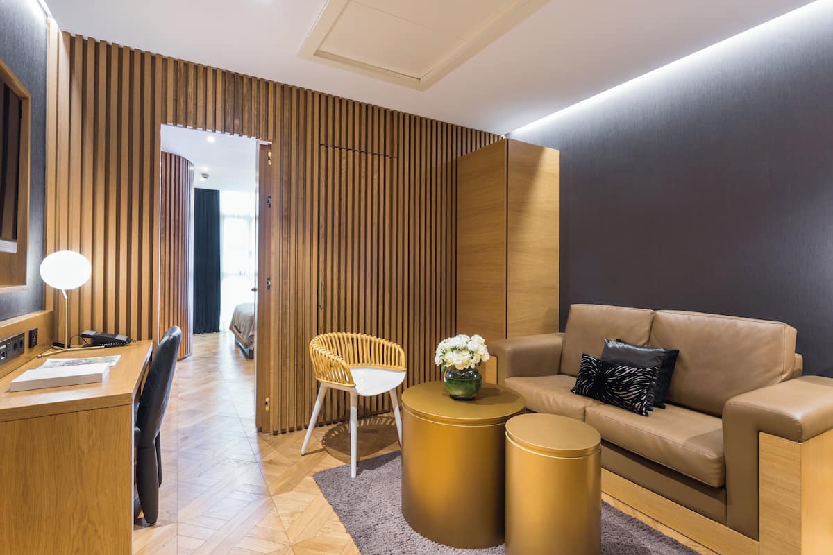 Una habitación de hotel moderna con una pared de acento de madera, un sofá, un escritorio con lámpara y una pequeña mesa redonda con un florero.