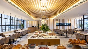 Un comedor moderno de hotel con barra de buffet, diseño de techo de madera y amplios ventanales.