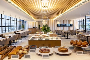 A modern hotel dining area with a buffet setup, wooden ceiling design, and large windows. - Monument Hotel (Barcelona)