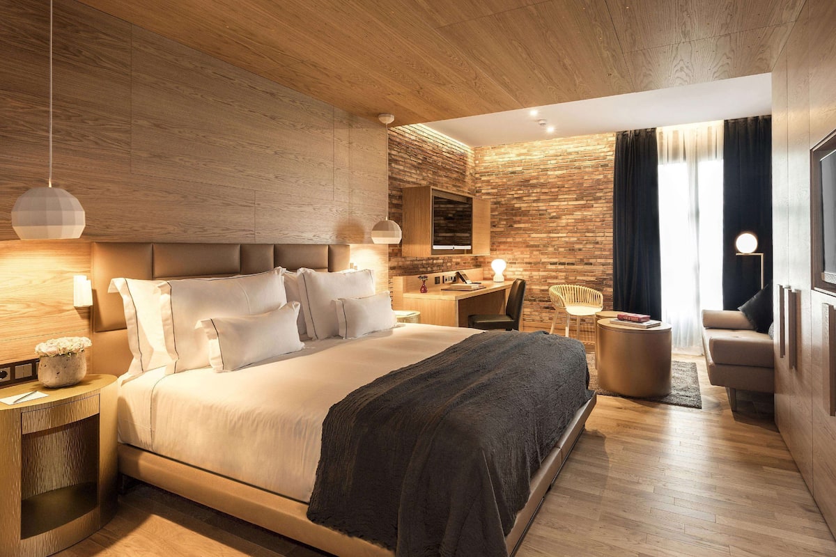 Una habitación de hotel moderna con una cama grande, un escritorio, un televisor y una zona de estar.