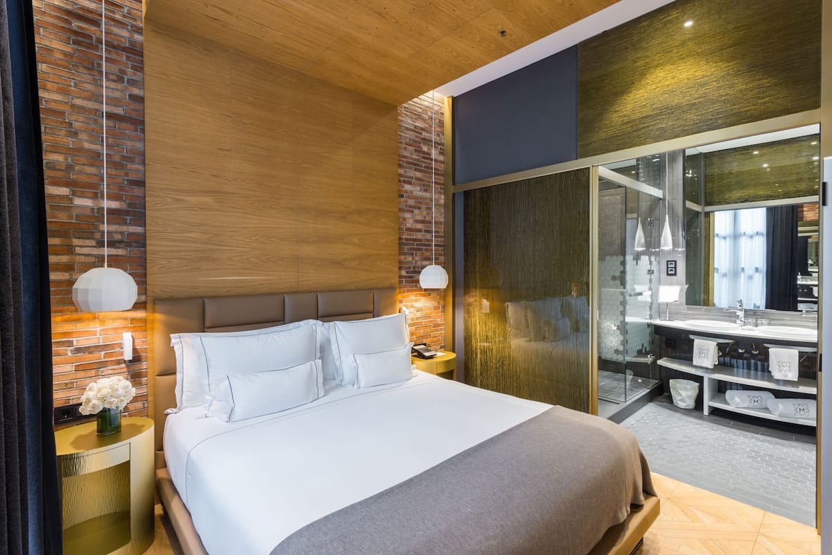 Habitación de hotel moderna con una cama grande, cabina de ducha de vidrio y pared de ladrillo.