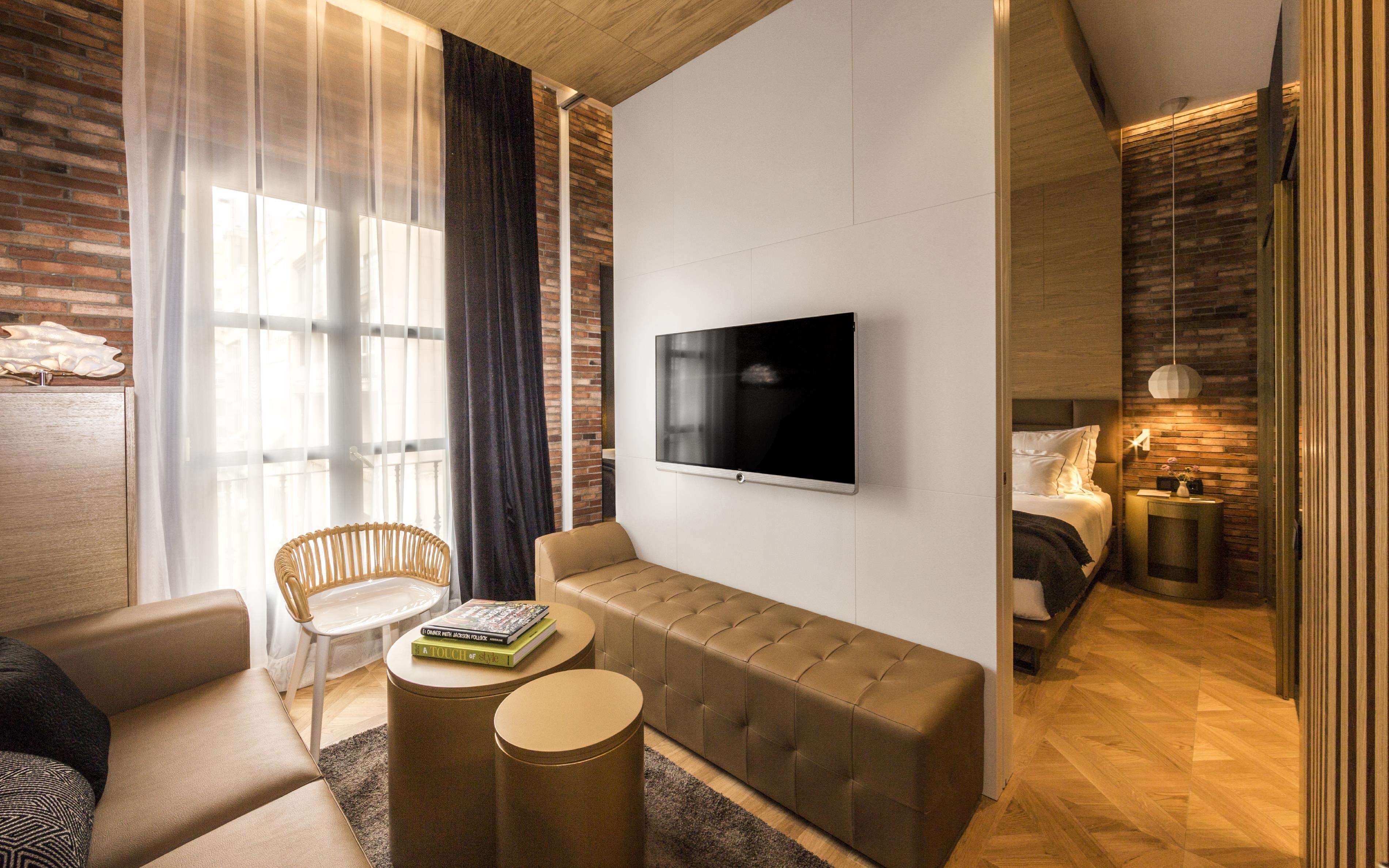 A modern hotel room with a sofa, a television, a small table, and a bed.