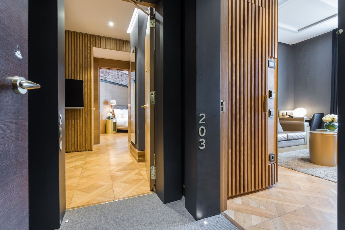 Un moderno vestíbulo de hotel con un mostrador de recepción de madera, una pantalla digital y una zona de sofás con un jarrón de flores.