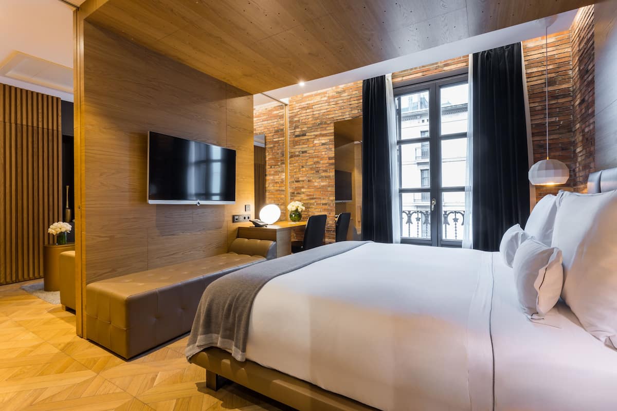 Una habitación de hotel moderna con una cama grande, un área de descanso, un escritorio y un televisor montado en la pared.