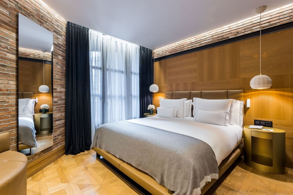 Una habitación de hotel moderna con una cama grande, un espejo, una mesita de noche y un cabecero de madera.