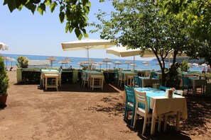 An outdoor dining area with tables and chairs, umbrellas, and a view of the beach and sea. - Ikiz Villas (Kemer)