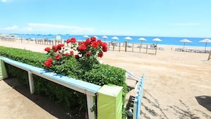 A beach with a row of red flowers, a white fence, and beach umbrellas. - Ikiz Villas (Kemer)