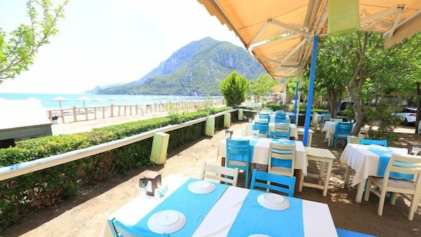 An outdoor dining area with tables and chairs, overlooking a beach and a mountain. - Ikiz Villas (Kemer)