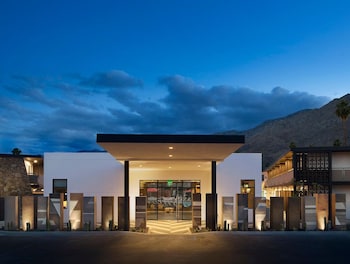 Hanging wicker pendant lights with bulbs, a stone wall, and greenery. at V Capri Palm Springs, a Dolce by Wyndham