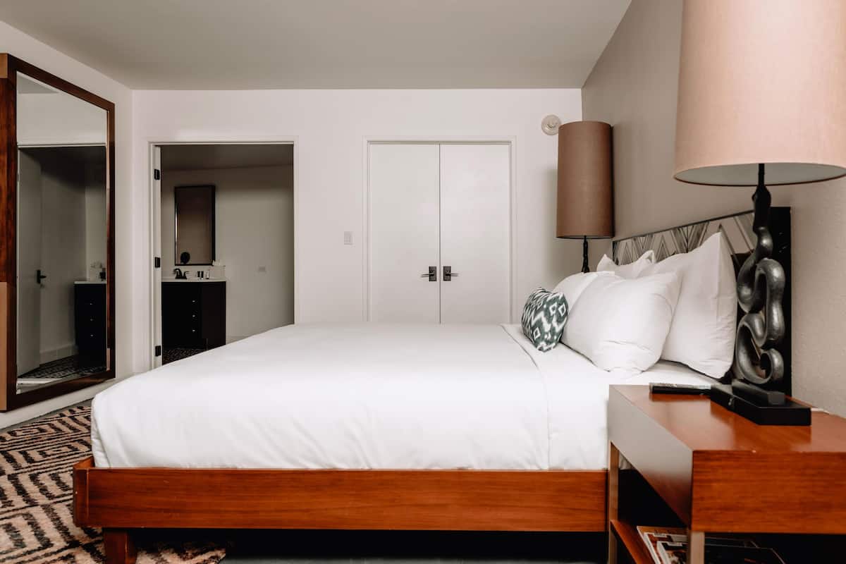Un dormitorio ordenado con una cama de madera, una mesita de noche, una lámpara y un armario.