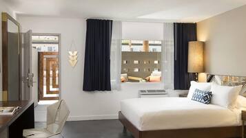 A hotel room with a bed, a desk, a chair, a window with curtains, and a lamp.