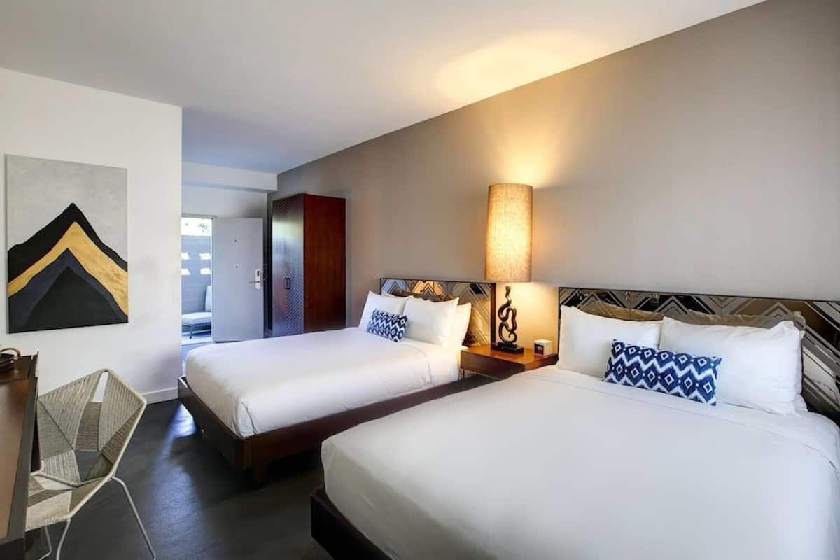 Habitación de hotel con dos camas, un escritorio, una silla y una lámpara de pared.