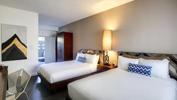 A hotel room with two beds, a desk, a chair, and a wall-mounted lamp.