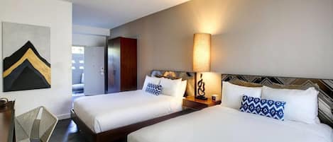 Habitación de hotel con dos camas, un escritorio, una silla y una lámpara de pared.