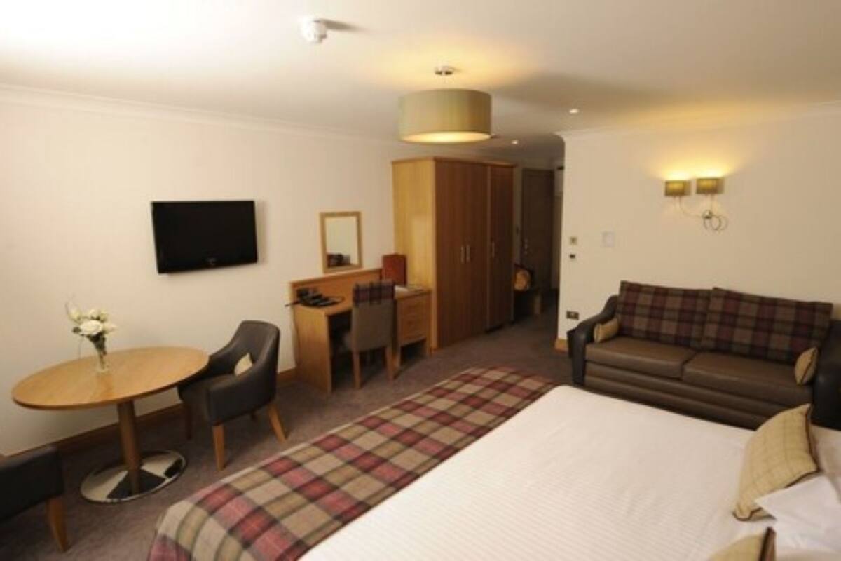 A hotel room with a bed, a desk, a chair, a sofa, a television, and a wardrobe.
