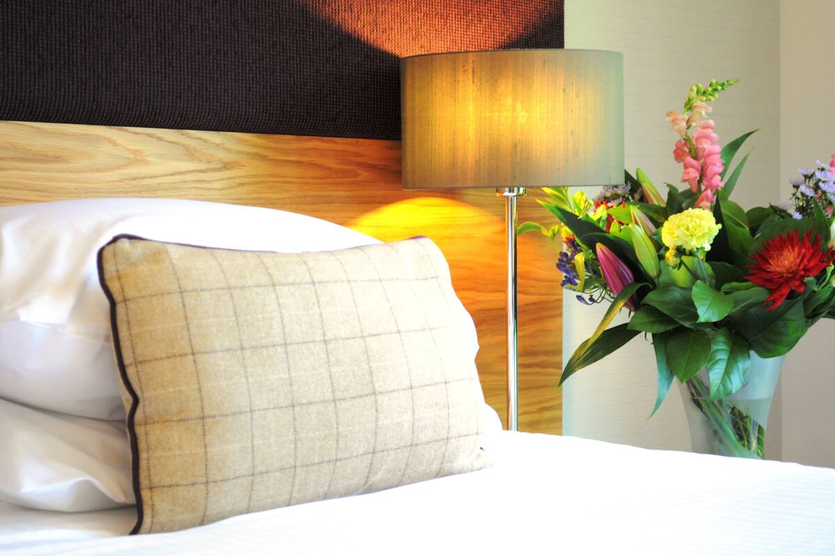 A hotel room with a bed, a lamp, and a floral arrangement.