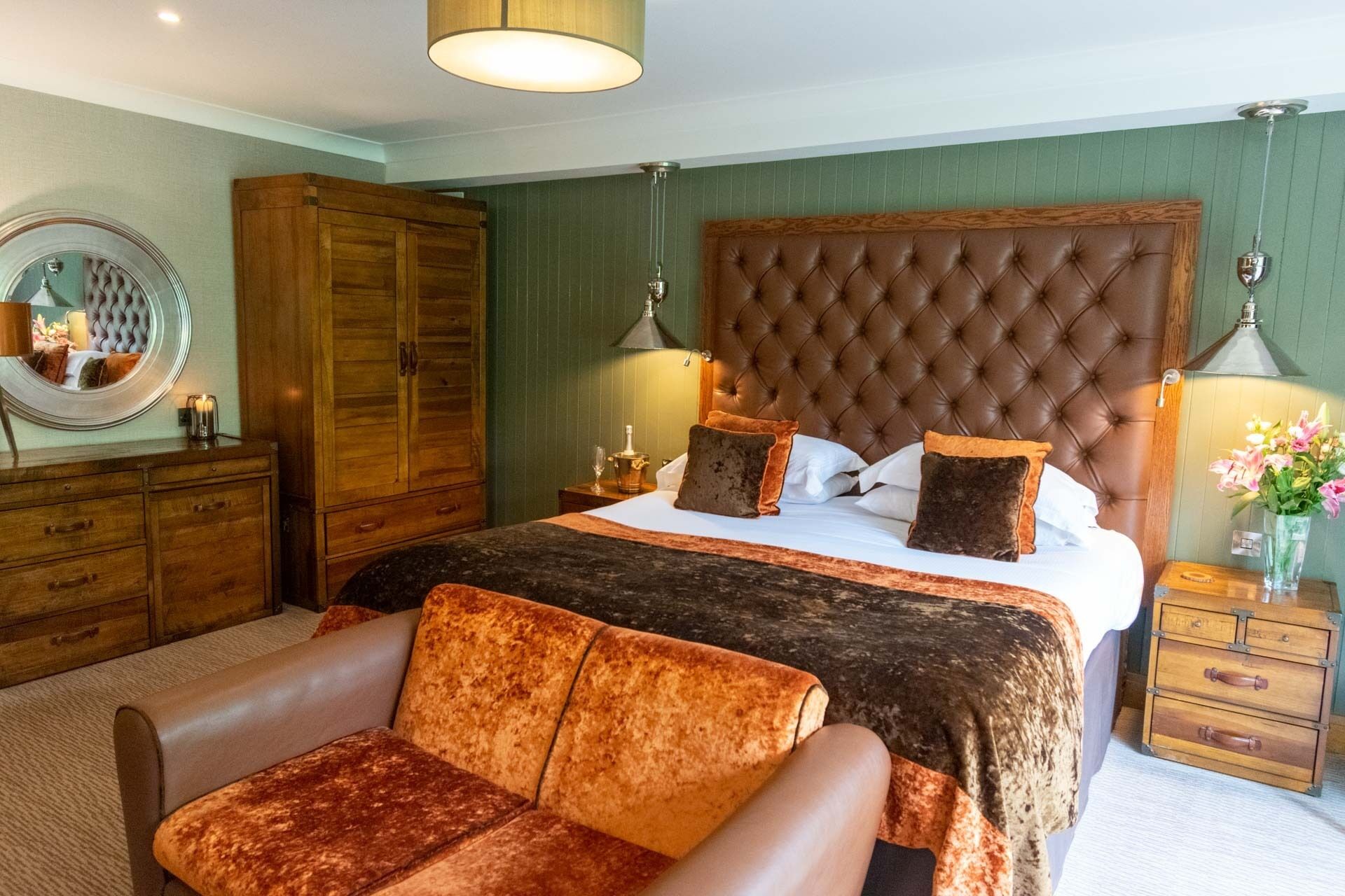 A bedroom with a large bed, wooden wardrobe, and a sitting area.
