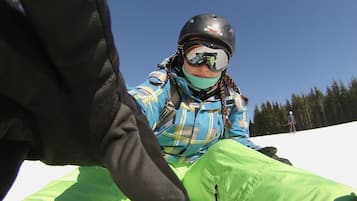 A person sitting on a white surface, wearing a helmet, goggles, and a plaid jacket.