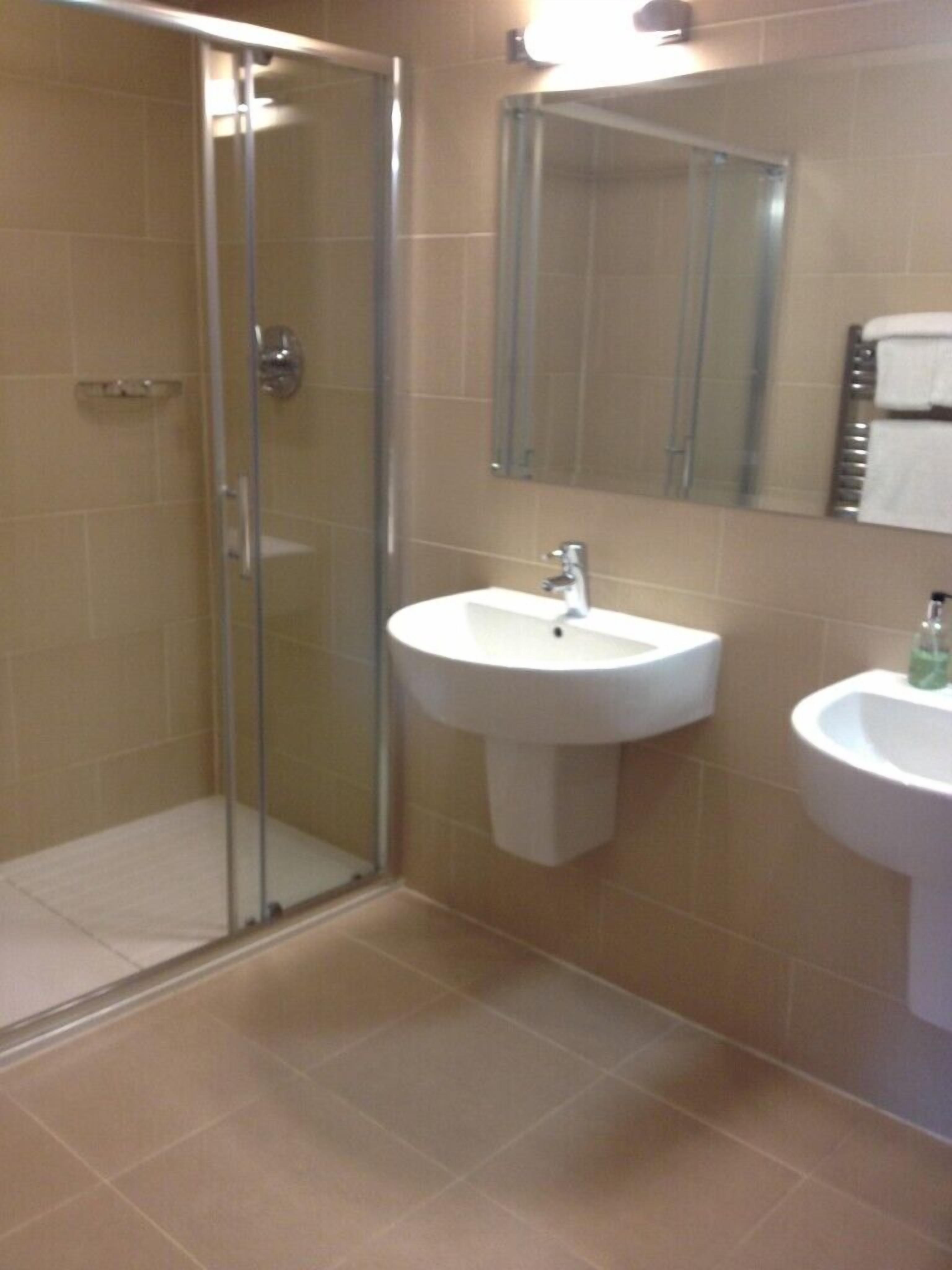 A bathroom with a glass shower enclosure, a sink, and a mirror.