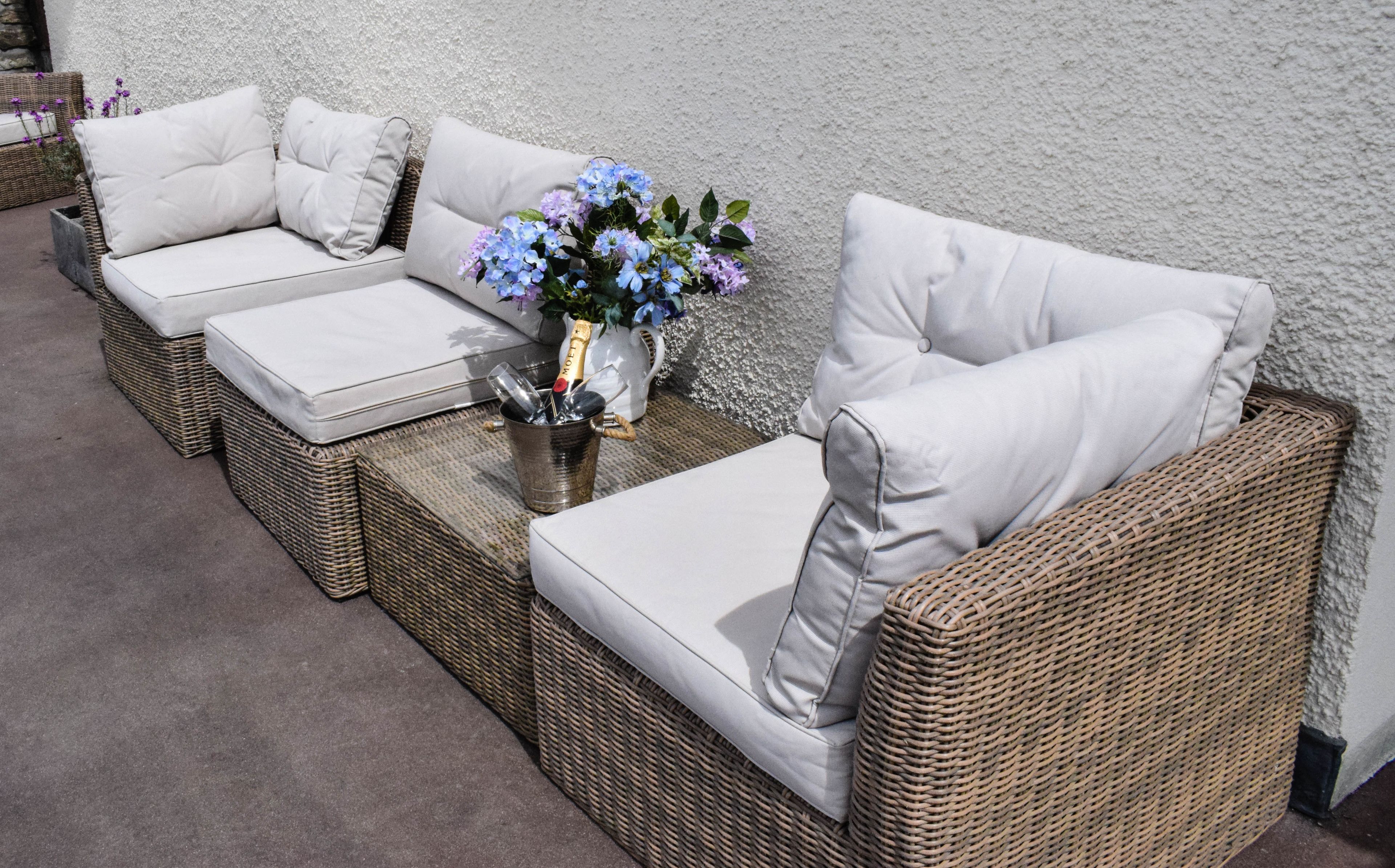 A wicker sofa set with cushions, a vase with flowers, and a bottle of champagne.