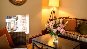 A cozy living room with a checkered sofa, a coffee table with a vase of flowers, a lamp, and a mirror on the wall. - Craigmhor Lodge & Courtyard (Pitlochry)