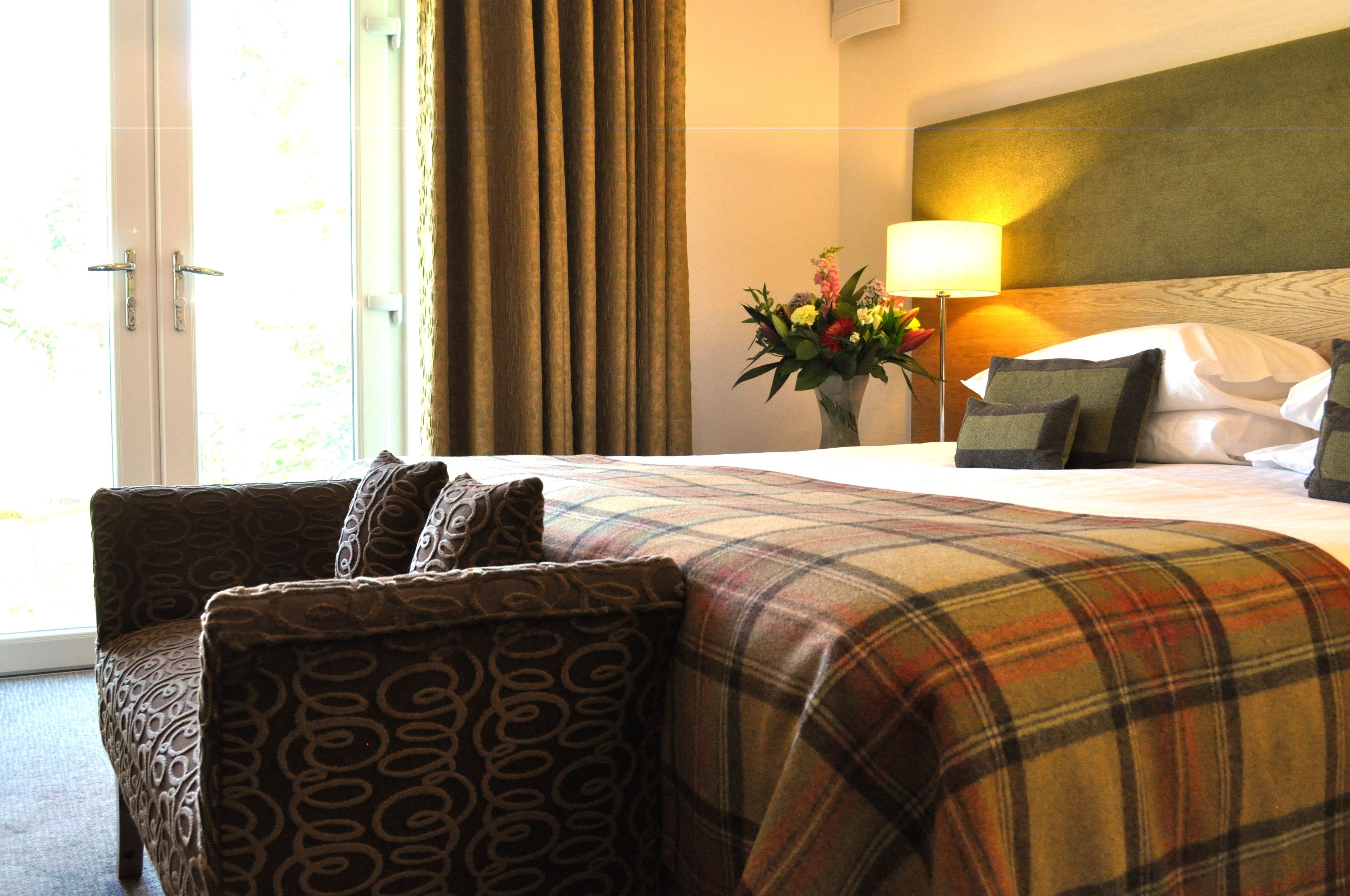 A hotel room with a bed, a chair, a lamp, and a window with curtains.