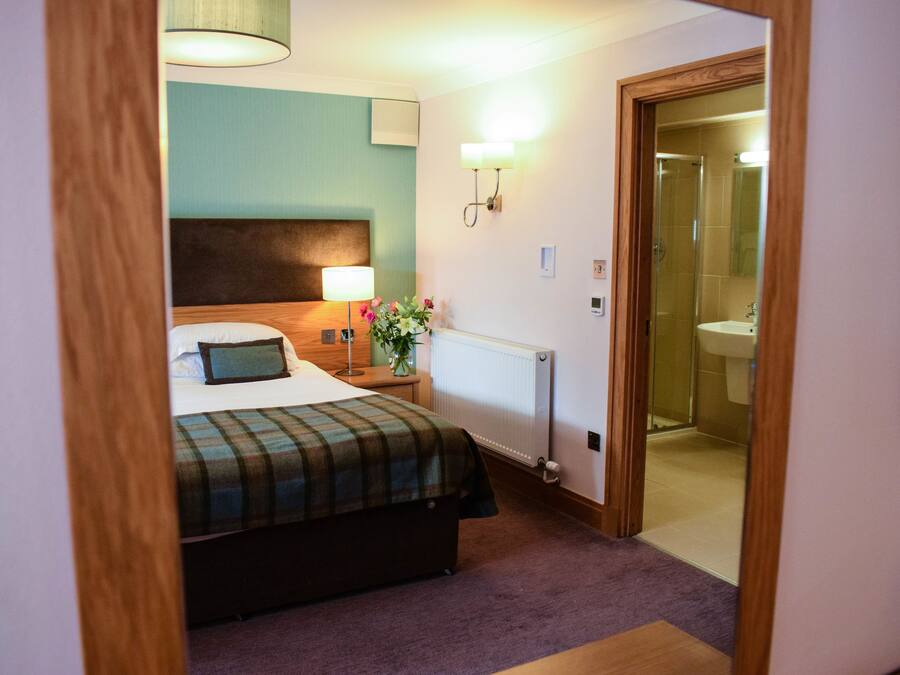A hotel room with a bed, bedside lamp, nightstand, and a view into the bathroom.