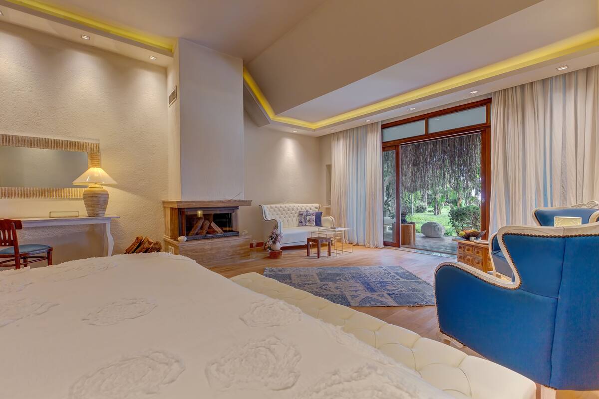 Quarto espaçoso com uma cama grande, uma poltrona azul, lareira e vista para o exterior.