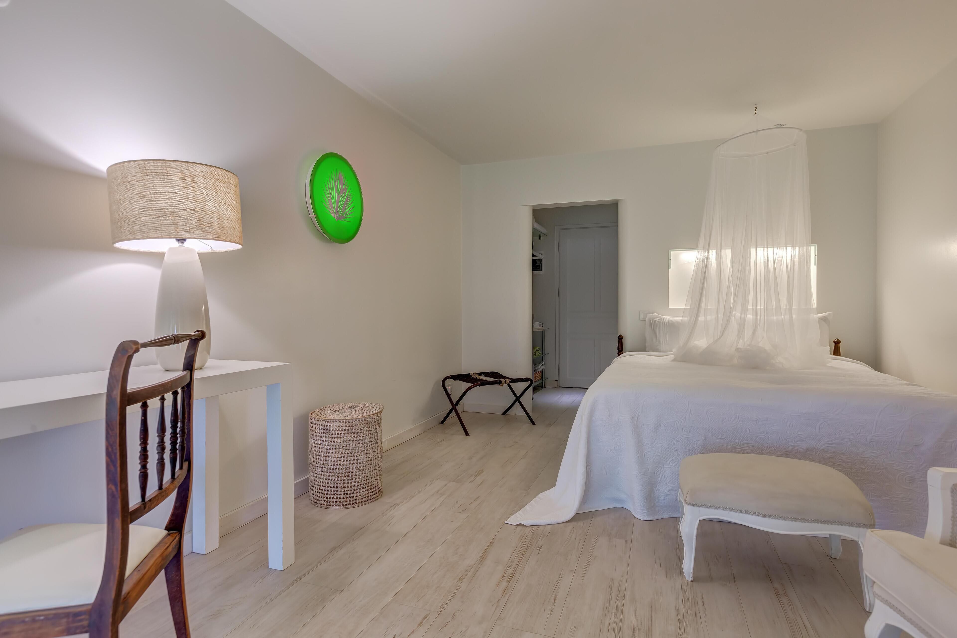 Un dormitorio con una cama, una silla, un escritorio, una lámpara y un adorno verde en la pared.